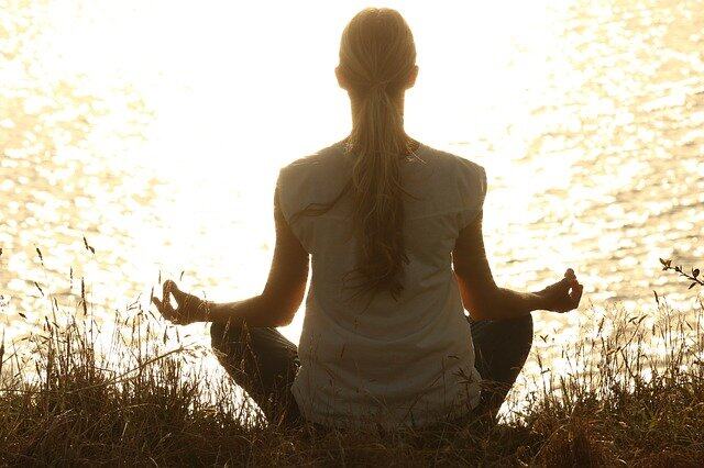 Woman in front of a lake meditating - self improvement